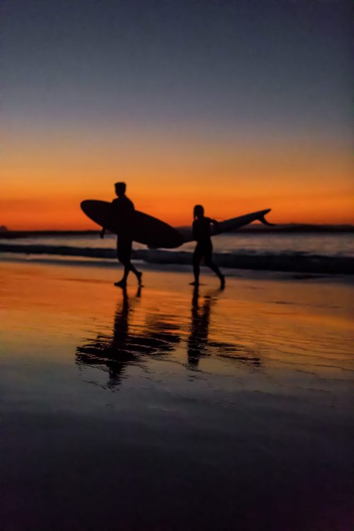 Surfers wearing earplugs on the beach at sunset